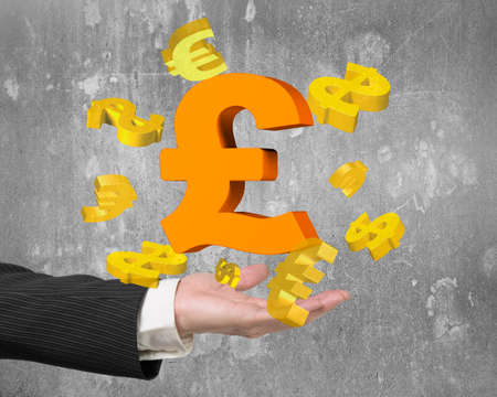 Man hand showing golden pound sterling symbol with dollar and euro signs, on gray concrete wall background.の写真素材