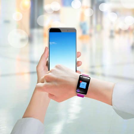 Woman hand holding smart phone and wearing smart watch with email icon on black touchscreen, on blur...