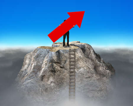 Man holding red arrow up sign, standing on top of dollar symbol shape mountain peak.の写真素材