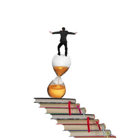 Businessman balancing on hourglass and stack of books, isolated on white background.の写真素材