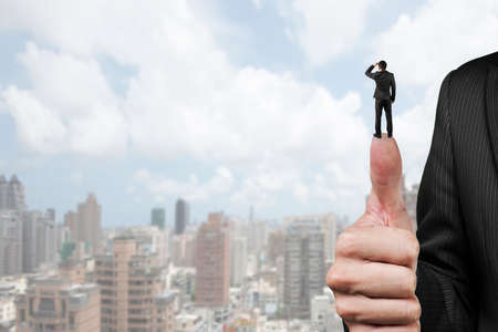 Businessman standing on top of another big thumb, with cloudy sky cityscape background.の写真素材