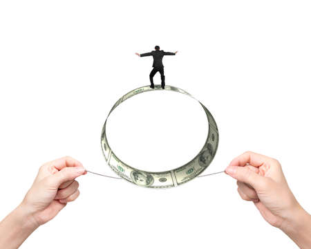 Two hands pulling rope with businessman balancing on roll of dollar bills, isolated on white.