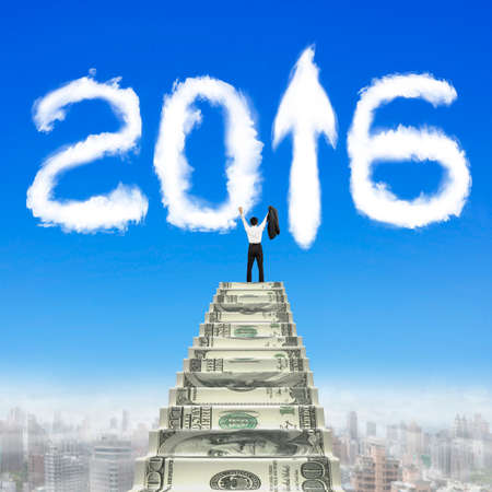 Businessman steps up money stairs with white 2016 arrow up shape clouds in blue sky.