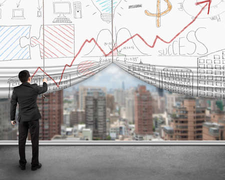 Businessman pulling open business doodles curtain with view of city buildings, standing on concrete floor.の写真素材