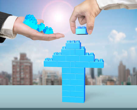 One hand holding blue stack blocks to the other hand completing arrow up shape on table, with city...
