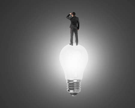 Businessman standing on light bulb with bright white light, on black background.の写真素材