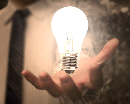 Businessman hand holding lightbulb with bright light, on business concepts doodles concrete wall...