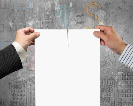 Two man's hands holding the tearing contract paper with blank white, on business concept doodles concrete wall background.の写真素材