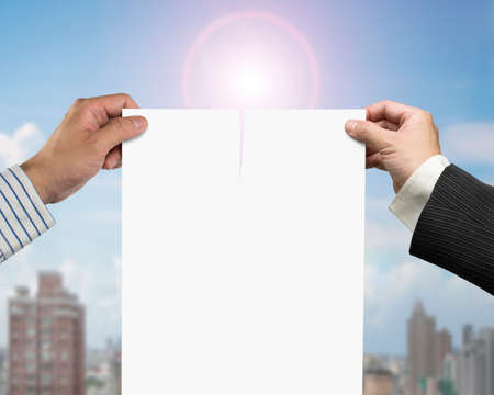 Two man's hands holding the tearing contract paper with blank white, on sunlight and city buildings background.の写真素材
