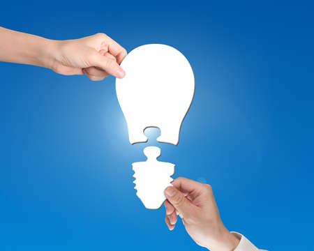 Woman and man two hands assembling one bulb shape puzzle of two jigsaw pieces, isolated on white.の写真素材