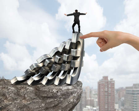 Businessman balancing on falling of Euro currency symbols with big woman hand forefinger helping on cliff, with sky clouds cityscape background. Domino effect and problem solving of concepts.の写真素材