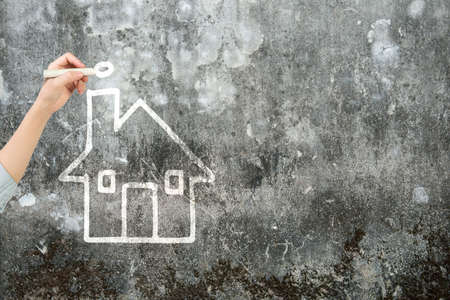 Woman hand holding chalk drawing house shape clouds on dirty concrete wall.の写真素材