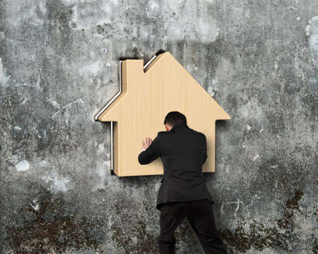 Man pushing wooden house into hole of old mottled concrete wallの写真素材