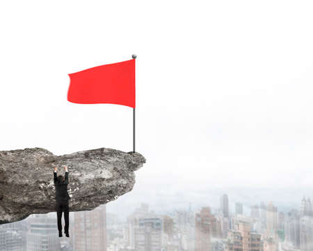 Wavy red flag on top of cliff with Businessman hanging mist city view backgroundの写真素材