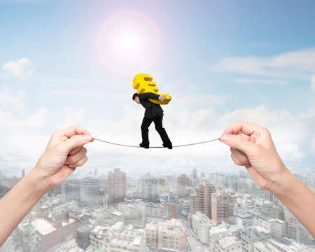 Man carrying golden Euro sign, balancing on tightrope with woman hands holding two sides, on cityscape background.の写真素材