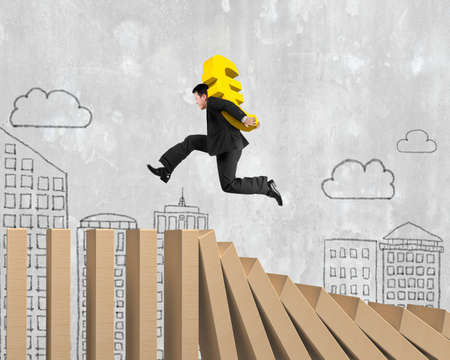 Man carrying golden Euro sign running on falling wooden dominos, with doodles concrete wall background.の写真素材