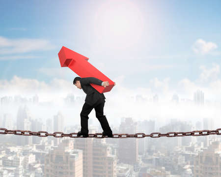 Businessman carrying red arrow sign balancing on rusty chain, with white background.