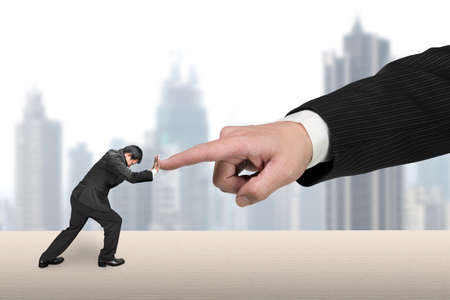 Small man pushing against big man hand forefinger on table, with city skyscraper background.の写真素材