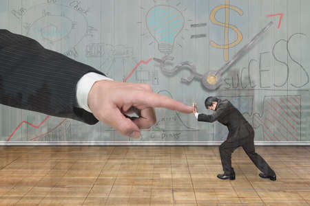 Small man pushing against big man hand forefinger, with business concept doodles wooden wall background.の写真素材