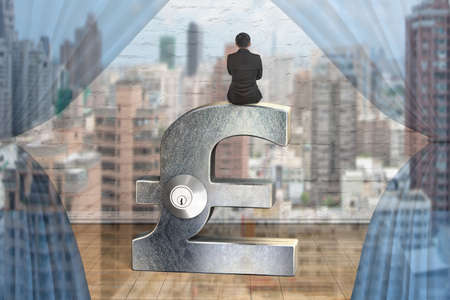 Rear view of businessman sitting on silver pound symbol with lockの写真素材
