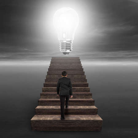 Glowing bulb on top of old wooden stairs with businessman climbing.の写真素材