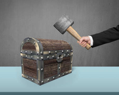 Hand holding hammer to hit old treasure chest on desk.の写真素材