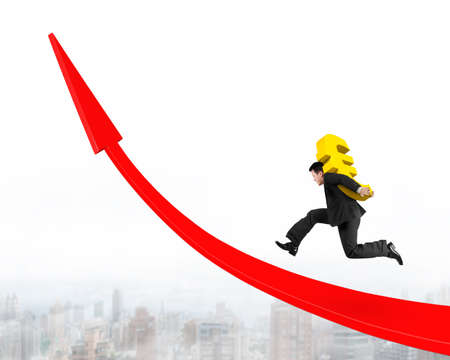 Businessman carrying golden Euro sign running on red arrow up graph, on city skyline background.の写真素材
