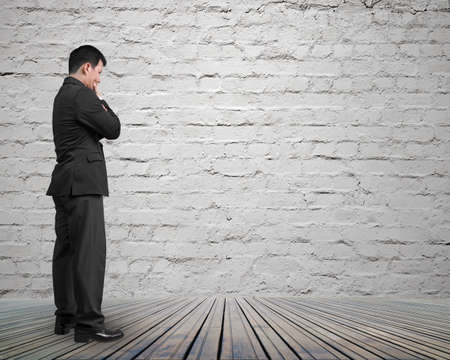 Standing businessman holding hand on chin and thinking, on brick wall and wooden floor background.の写真素材