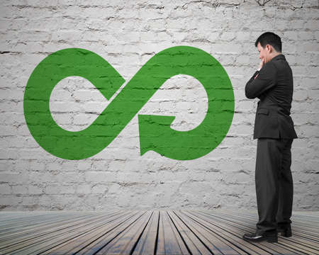 Green circular economy concept. Arrow infinity symbol on brick wall with man thinking.の写真素材