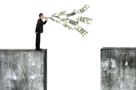 Man using megaphone yelling with dollar bills spraying out, on top of high concrete wall, isolated on white.の写真素材