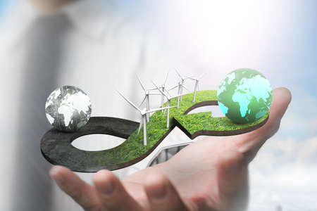 Green circular economy concept. Hand showing arrow infinity symbol of grass texture with wind turbines and two globes of different colors.の写真素材