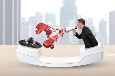Telephone handset with businessman using megaphone spraying out 3D thumbs down objects, yelling at another man.の写真素材