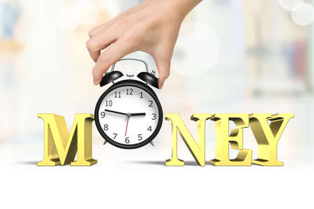 Time is money concept. Woman hand holding alarm clock with gold money word.の写真素材