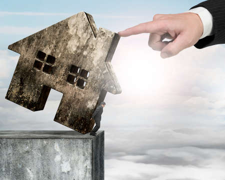 Man holding old dirty concrete house at edge of high concrete wall with another big hand helping to...