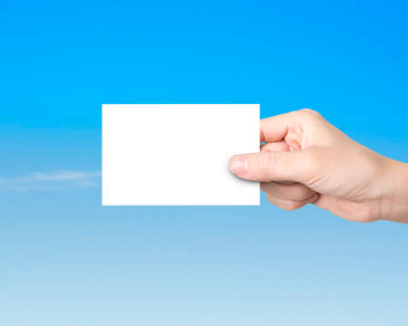 Woman hand holding blank white paper, on blue sky backgroundの写真素材