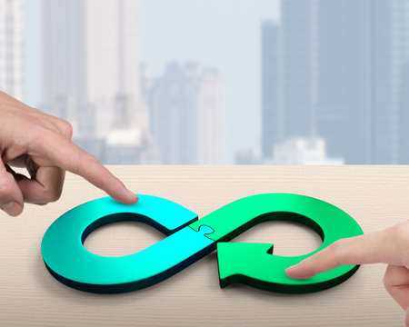 Circular economy concept. Two hands assembling arrow infinity recycling symbol of jigsaw puzzle pieces, isolated on white background.の写真素材