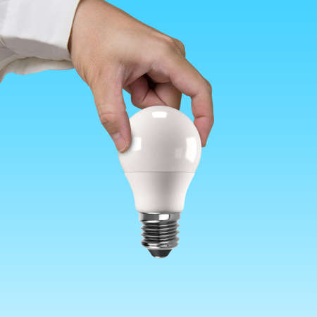 Hand holding one LED bulb, isolated on blue background. Energy saving concept.