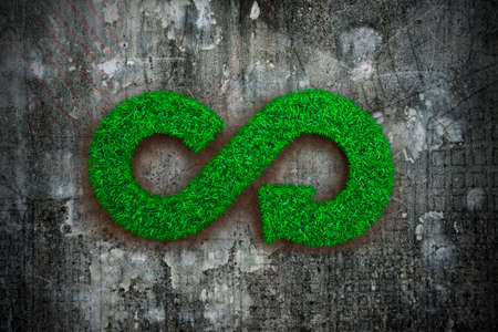 ECO and circular economy concept. The green grass in form of arrow infinity recycling symbol on dirty concrete wall background.の写真素材