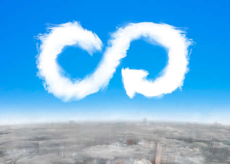ECO and circular economy concept. White clouds in arrow infinity recycling symbol shape in blue sky with cityscapes background.の写真素材