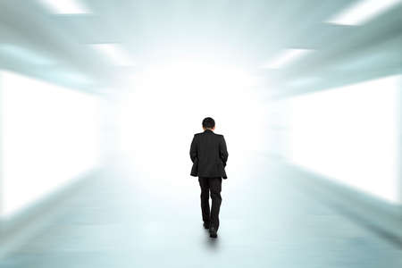 Rear view businessman walking through underpass toward bright side, with blank billboard advertising...