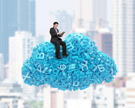 Big data and cloud computing concept. Sitting businessman using digital tablet on cloud of blue letters and numbers, on city buildings cityscape background.の写真素材