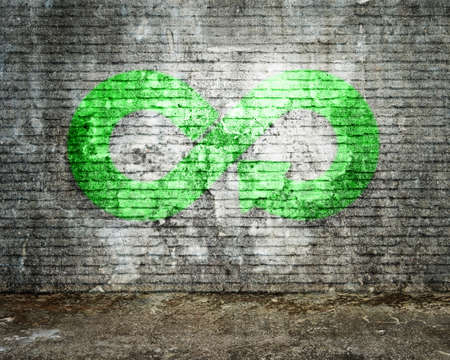 Green Eco-friendly and circular economy concept. Infinity arrow recycling symbol of fluorescent green graffiti paintings on dirty bricks wall with mottled concrete floor.の写真素材