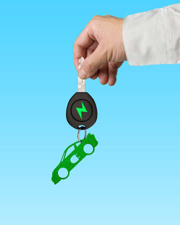 Green energy electric car and Eco-friendly environmental protection concept. Man hand holding electric car key with green leaves keyring in sports car shape, isolated on blue background.の写真素材