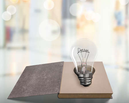 Opened old book with Dream word wire shape of light bulb on wooden table, isolated on blur background.の写真素材