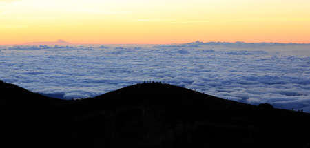 Silhouette of people waiting for the sunrise at the top of Mount Fuji with a sea of clouds behind