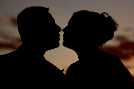 A couple silhouetted against a sunset the moment before the big kiss.の写真素材