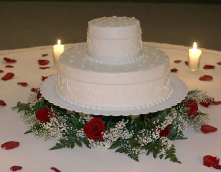 Two tiered wedding cake closeup surrounded by rose petals. Candles illuminate the cake for a effect.の写真素材