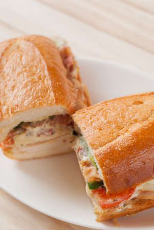 Close up of tasty french bread sandwich with smoked chicken and bacon salad cut in a half on a white dish.の写真素材