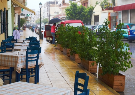 Empty tavern on a street in town of Zakynthos in rainy weather, in the background a man with an umbrella      のeditorial素材