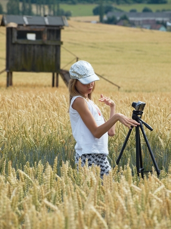 Teenage girl making selfie with a tripod in the field of ripening wheat.